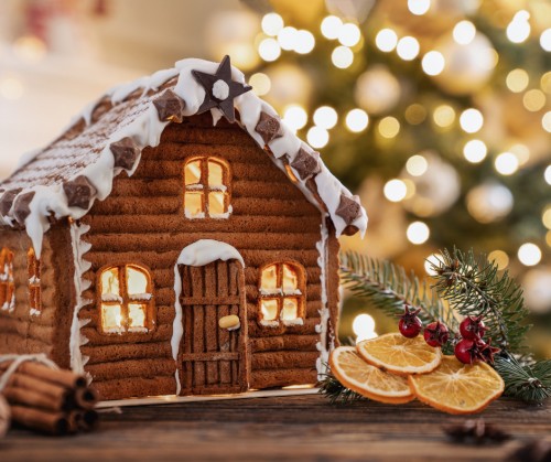 A photo of a ginger bread house with icing and Christmas motives. There is also a Christmas tree branch with dried up oranges.